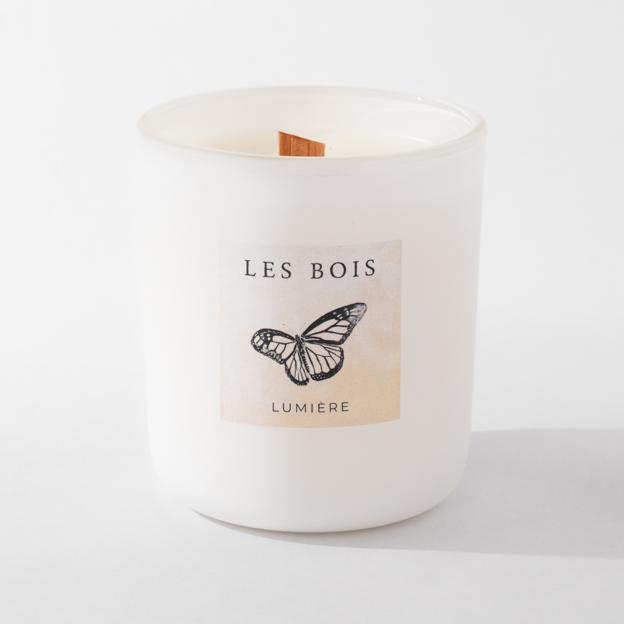White candle with 'Les Bois Lumiere' label featuring a butterfly on a white background
