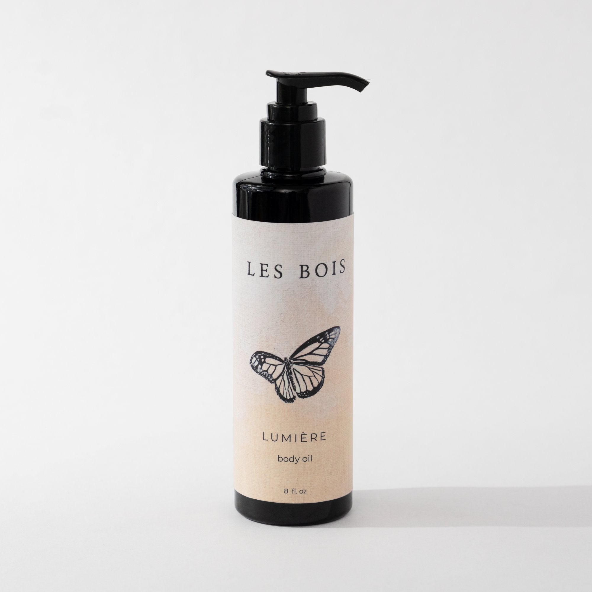 Bottle of Les Bois Lumérie body oil with a butterfly design on a white background
